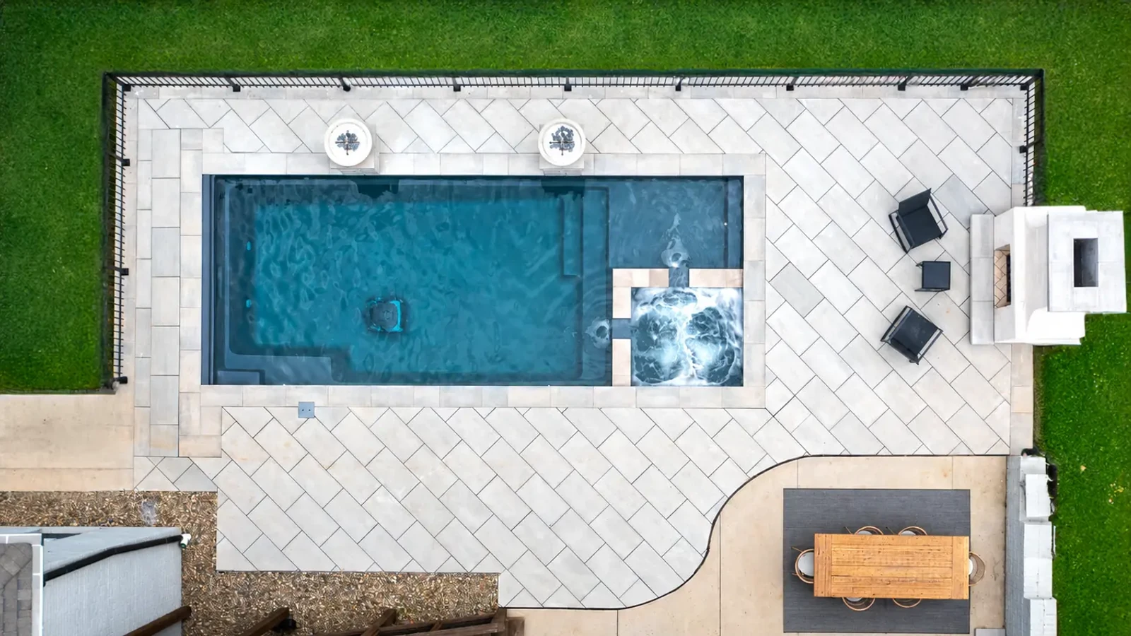 Overhead photograph of a rectangular swimming pool, spa, paved patio and outdoor seating.